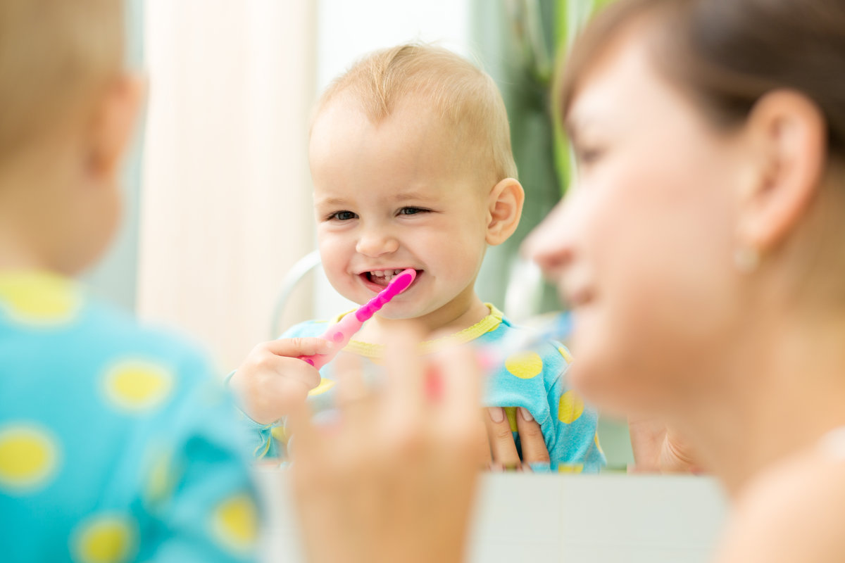 mother and kid girl look at mirror during teeth brushing
